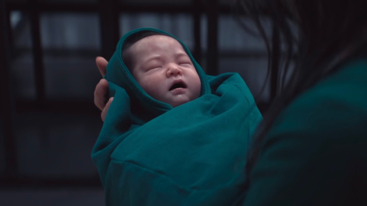 نوزاد تازه‌متولدشده در فصل سوم سریال Squid Game با لباس سبز، در آغوش مادرش پیش از ورود به بازی‌ها