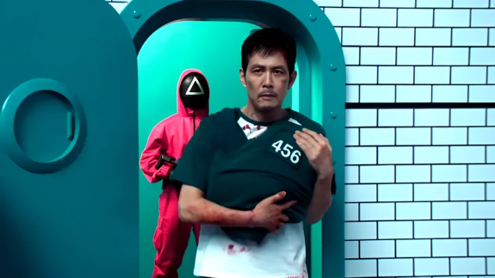 لی جونگ‌جه در نقش گی‌هون در پایان فصل سوم Squid Game، در حالی‌که نوزاد را در آغوش دارد و از در خروجی بازی‌ها عبور می‌کند