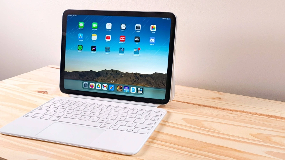 iPad 2025 متصل به صفحه‌کلید سفید اپل در حال اجرا روی میز چوبی