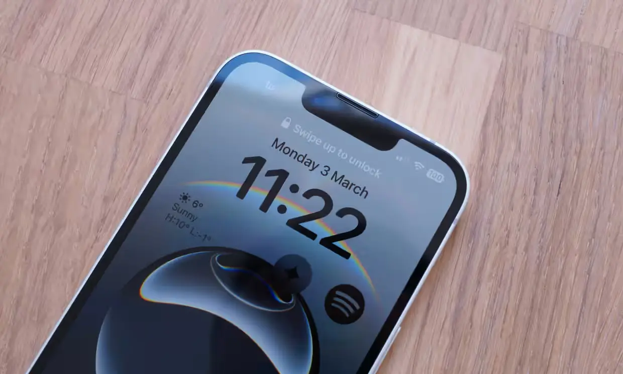 نمای نزدیک نمایشگر آیفون 16e — طراحی ناچ سنتی، بدون داینامیک آیلند، با رابط قفل iOS 18 و ساعت دیجیتال در مرکز صفحه